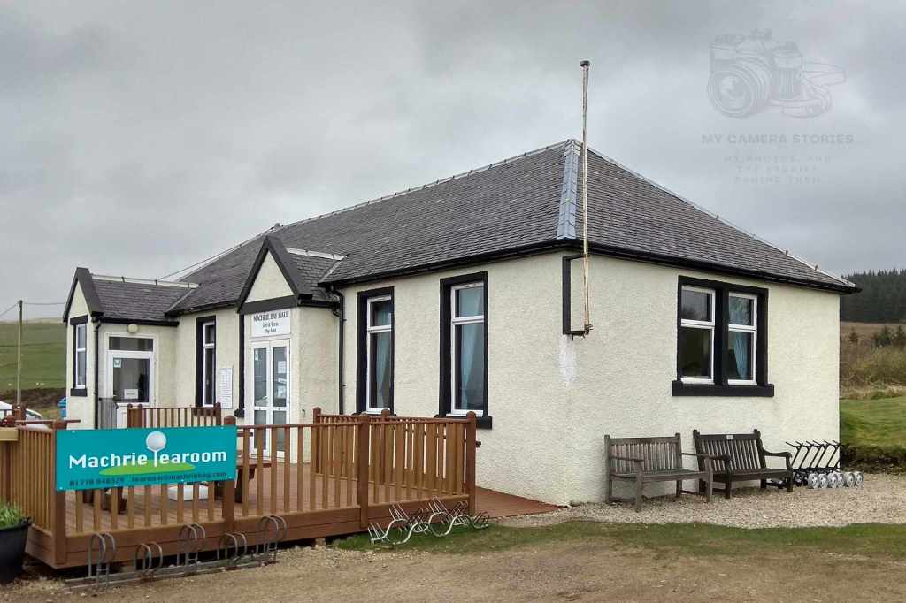 Exterior view of the Machrie Tearoom at Machrie Bay Golf Club on the Isle of Arran, Scotland, featuring a light-colored building with a sign and wooden decking.