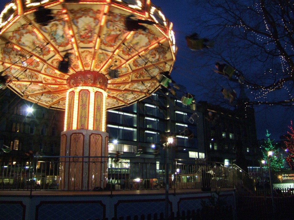 A beautifully illuminated carousel at night with colorful lights, surrounded by a festive setting and buildings in the background.