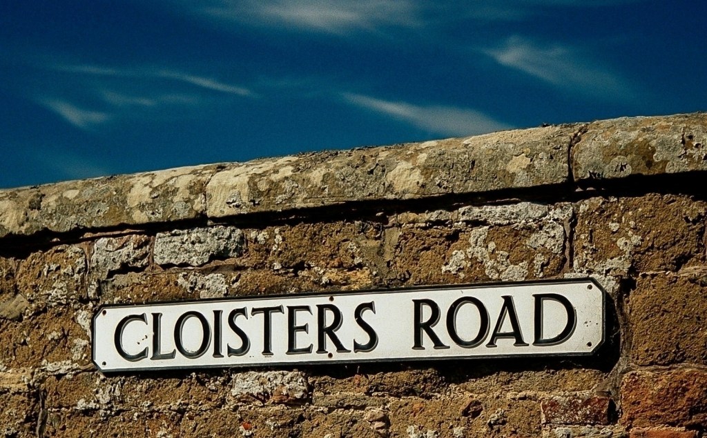 Sign for Cloisters Road on a stone wall with a blue sky in the background